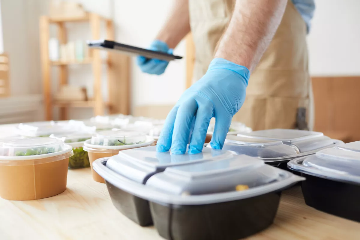 Profissional manuseando embalagens de refeições prontas em cozinha, ilustrando a aplicação do método cook & chill em restaurantes com foco em produção antecipada e segurança alimentar.