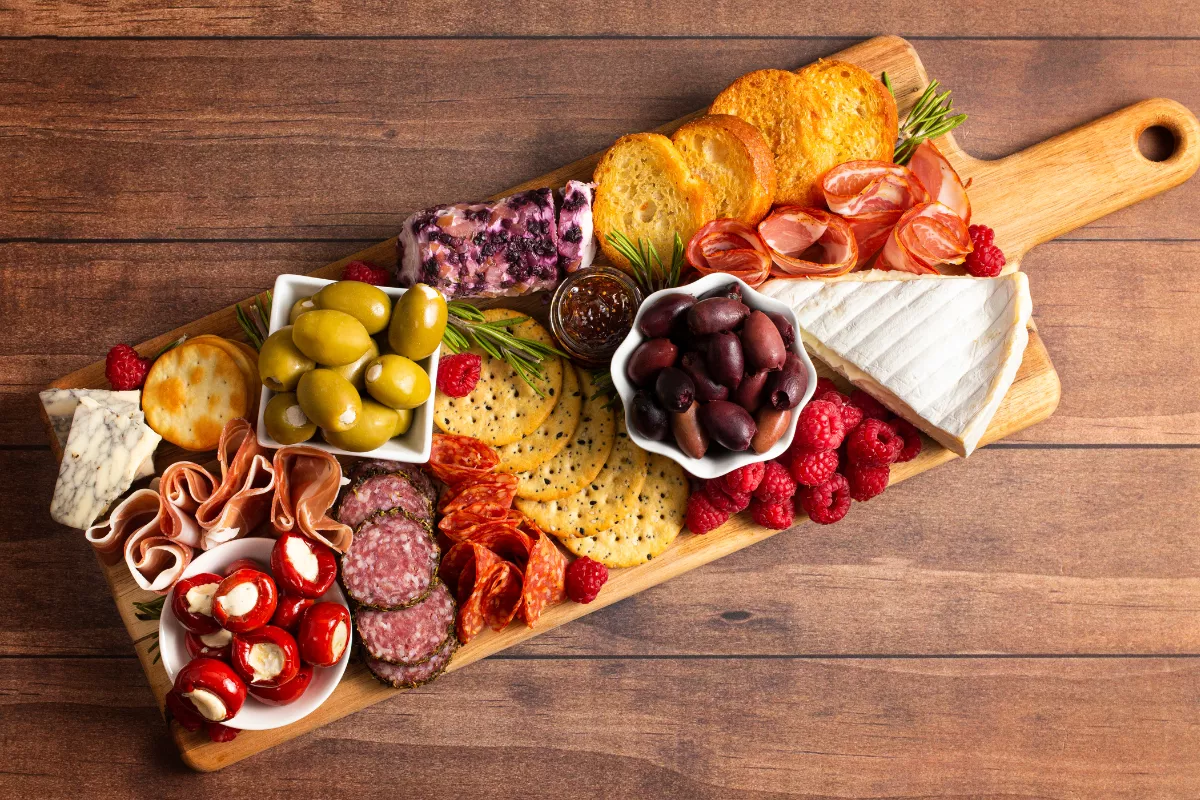 Tábua de frios e queijos com pães, frutas vermelhas, azeitonas, embutidos e patês servida sobre tábua de madeira — ideal como entrada compartilhável para cardápio de Dia dos Namorados.