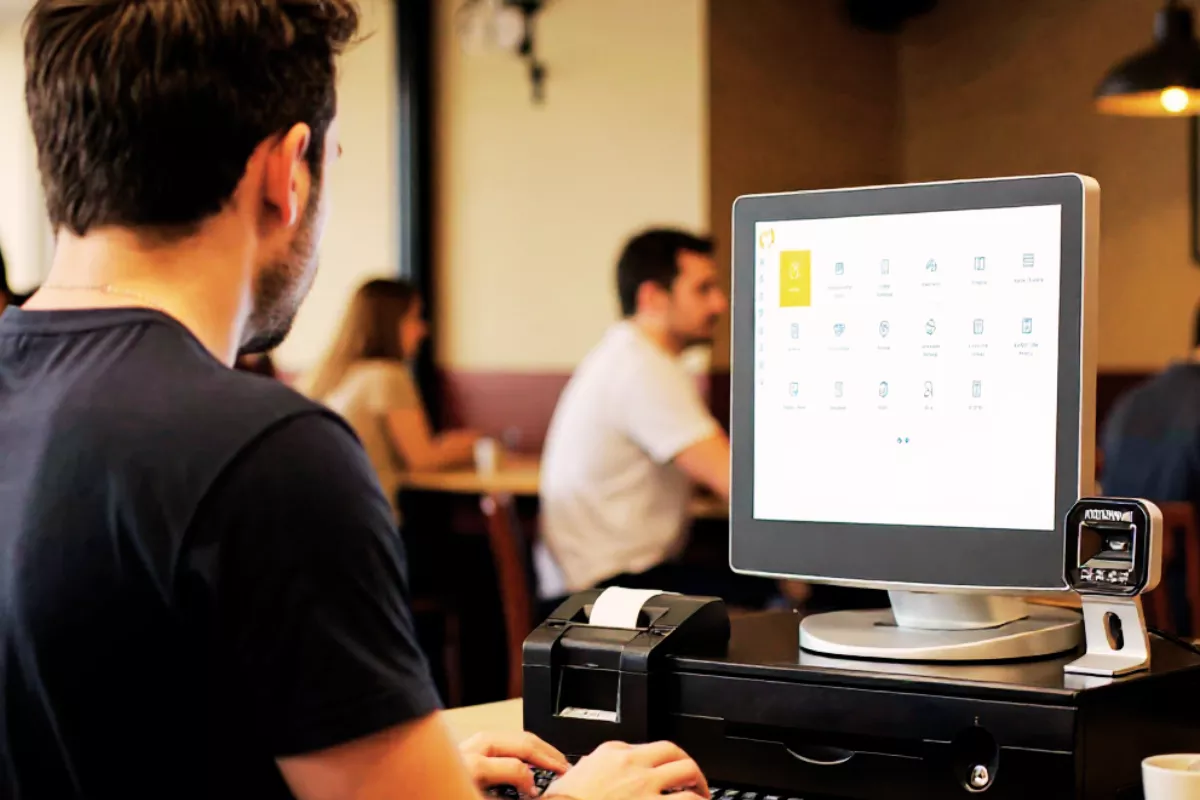 Funcionário de pastelaria operando um sistema de gestão em frente de caixa com interface do CNM, mostrando automação no atendimento ao cliente.