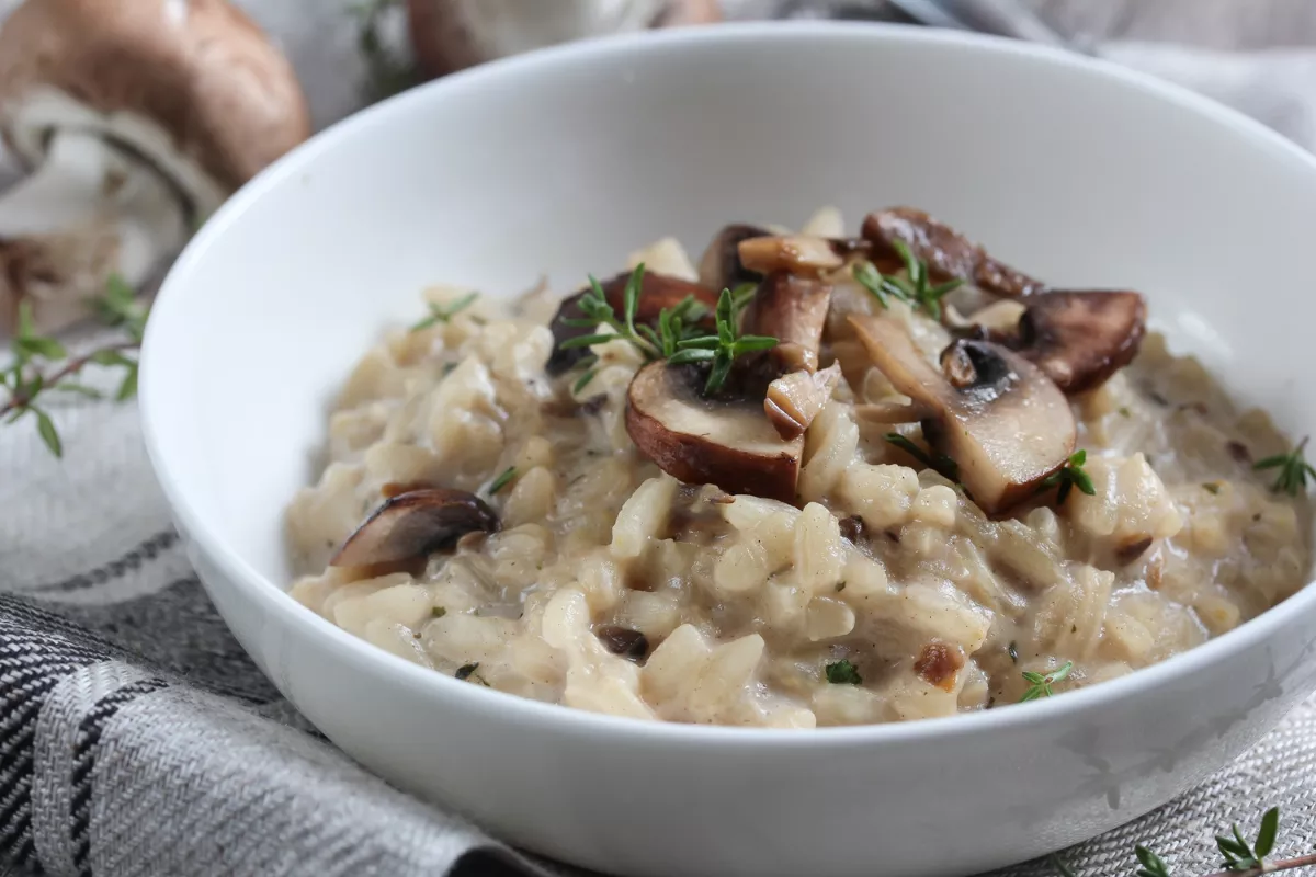 Risoto cremoso de cogumelos servido em prato branco, decorado com tomilho fresco, prato quente e sofisticado para cardápio de inverno de restaurante.
