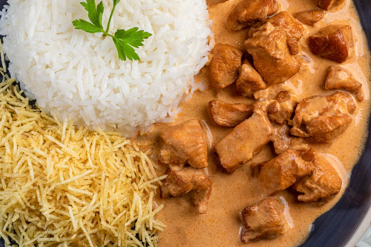 Strogonoff de frango ao molho cremoso servido com arroz branco e batata palha, combinação clássica do delivery em dias frios.