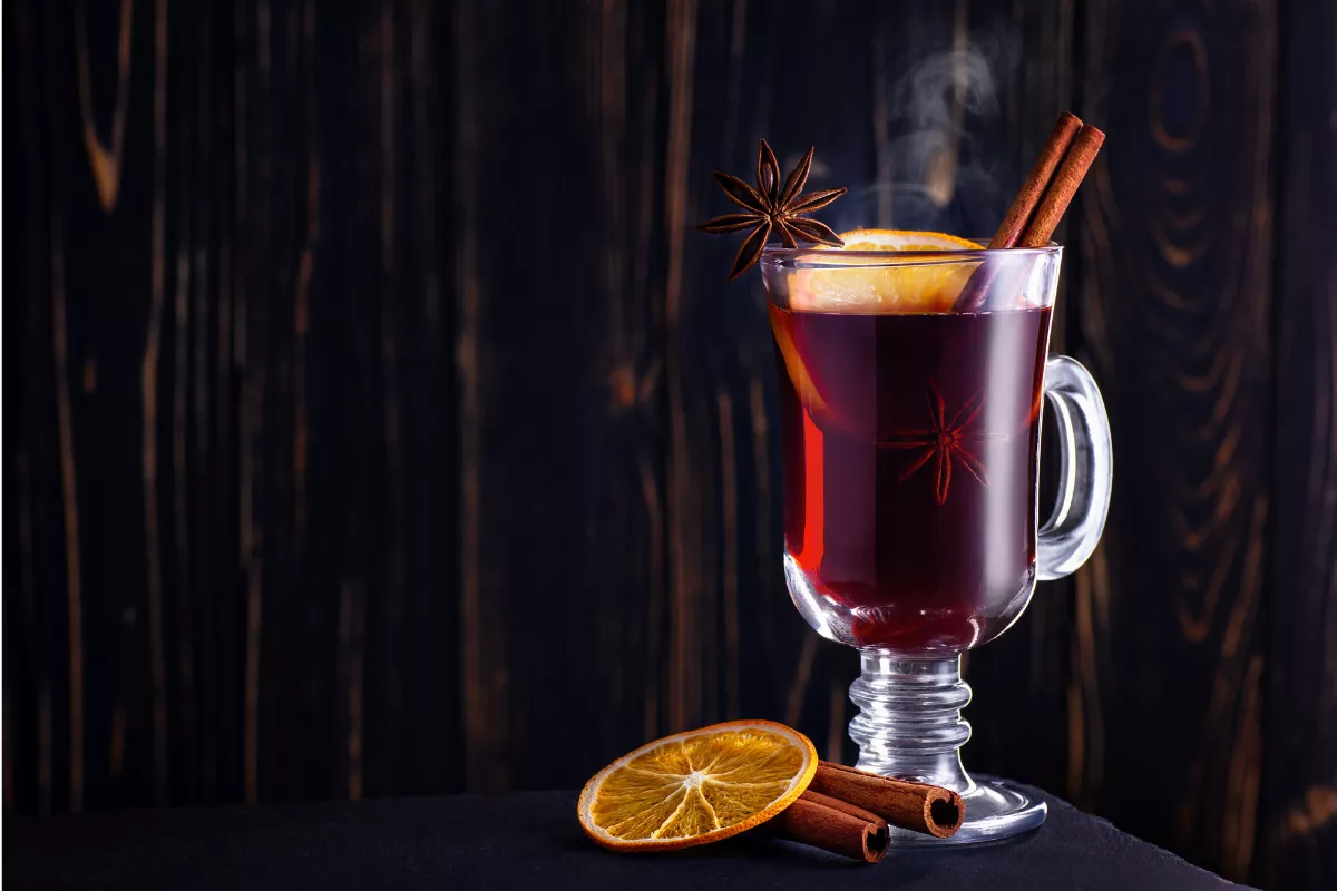 Copo de vidro com vinho quente, decorado com canela, anis-estrelado e fatia de laranja, bebida típica das festas juninas.