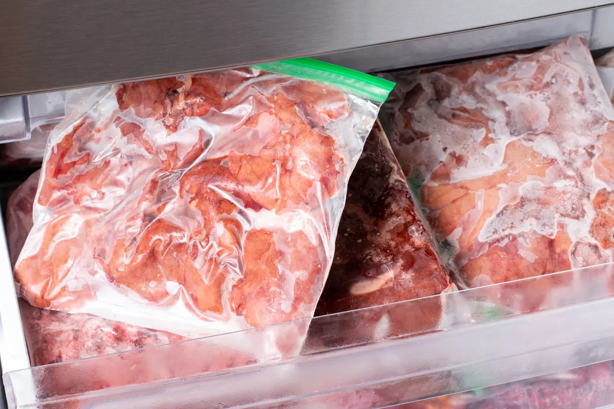Alimentos crus embalados a vácuo em saco plástico transparente, armazenados corretamente no freezer. Imagem ilustra boas práticas de armazenamento e temperatura exigidas pela Anvisa.