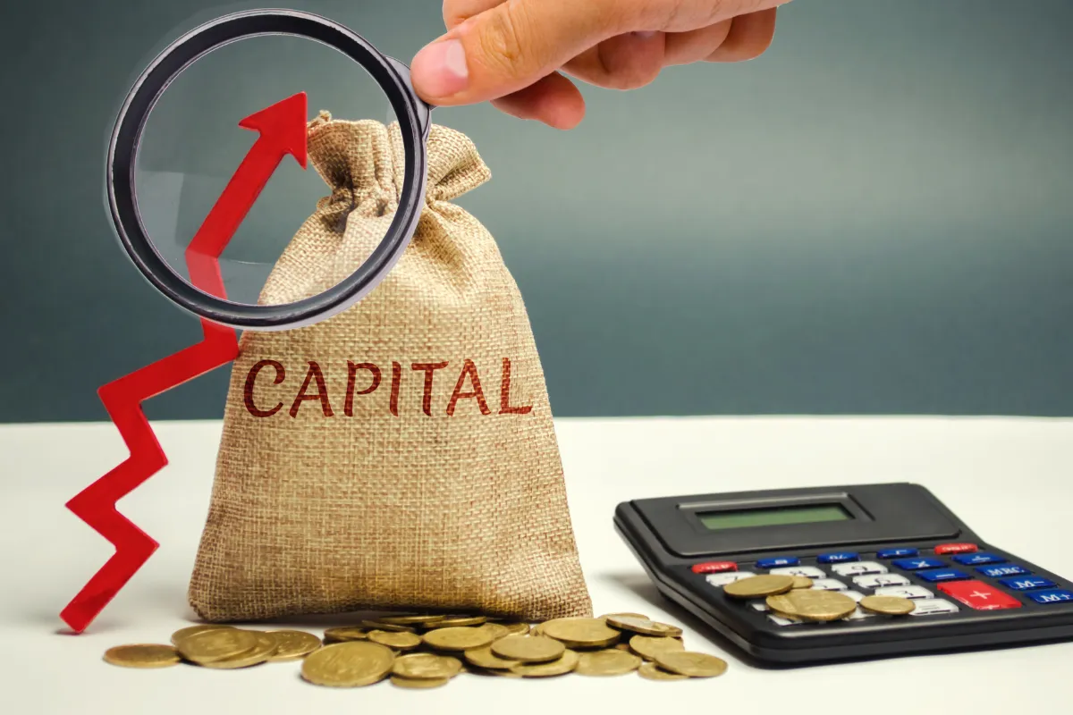 Saco de tecido com a palavra “capital”, cercado por moedas e uma calculadora, representando o capital de giro necessário para manter um restaurante funcionando nos primeiros meses.