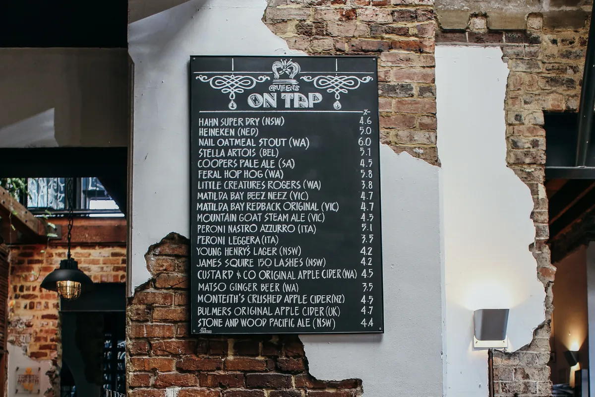 Cardápio de parede estilo lousa com letras escritas à mão em ambiente rústico, representando o menu visual e descolado de bares.