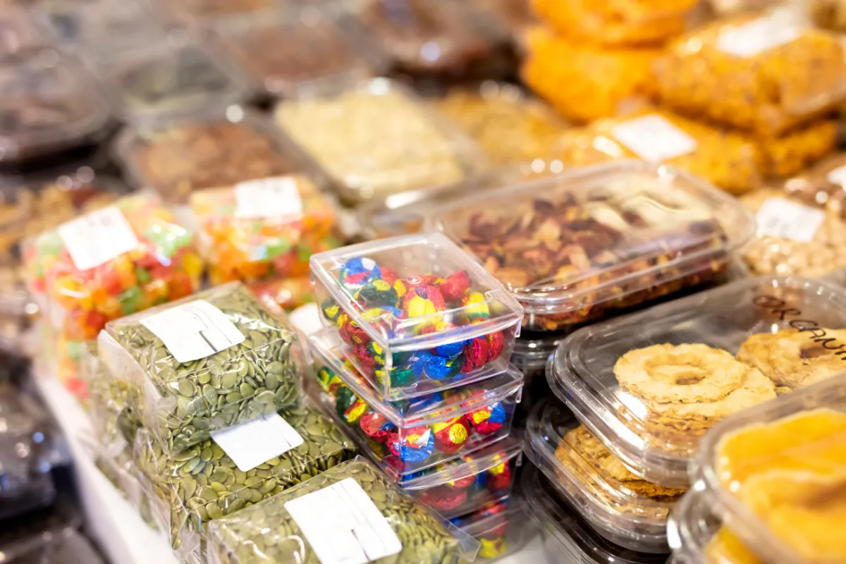 Embalagens plásticas com alimentos prontos e porcionados, como doces, sementes e snacks, organizadas em prateleira de autosserviço no estilo Grab and Go.