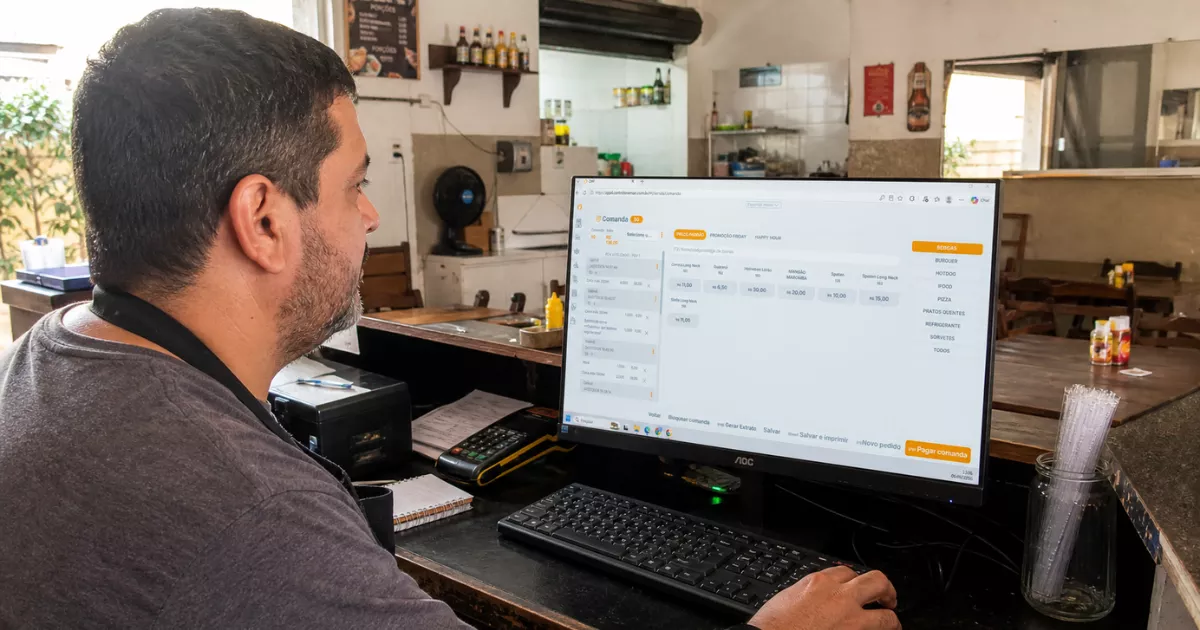 Dono de restaurante usando o PDV ControleNaMão em um computador no balcão do estabelecimento.