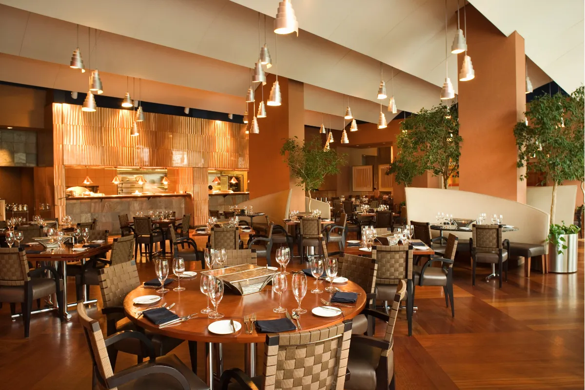 Interior sofisticado de restaurante com mesas postas, iluminação pendente e ambiente elegante pronto para receber clientes na inauguração.