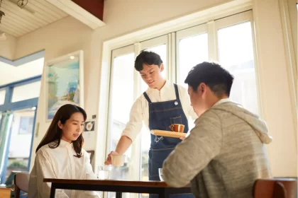 Garçom sorridente servindo bebida para casal em restaurante durante o dia, ilustrando atendimento cordial em estabelecimentos que costumam sugerir os 10% de taxa de serviço.