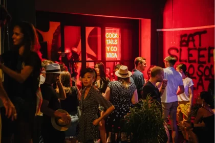 Pessoas reunidas em frente a bar com luz vermelha e letreiro de neon, ilustrando bares movimentados com atmosfera noturna e urbana.