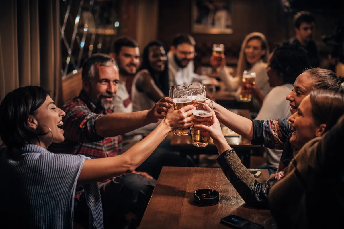 Grupo de amigos brindando com copos de cerveja em bar aconchegante, representando bares com clima descontraído e nomes que aproximam pessoas.