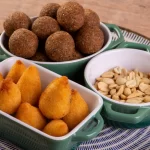 Prato com coxinhas, bolinhas de falafel e amendoins servidos em potes verdes, simbolizando variedade e qualidade em uma loja de salgados artesanal.