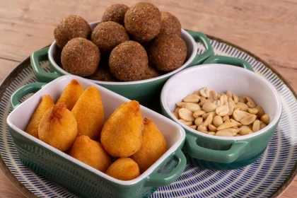 Prato com coxinhas, bolinhas de falafel e amendoins servidos em potes verdes, simbolizando variedade e qualidade em uma loja de salgados artesanal.