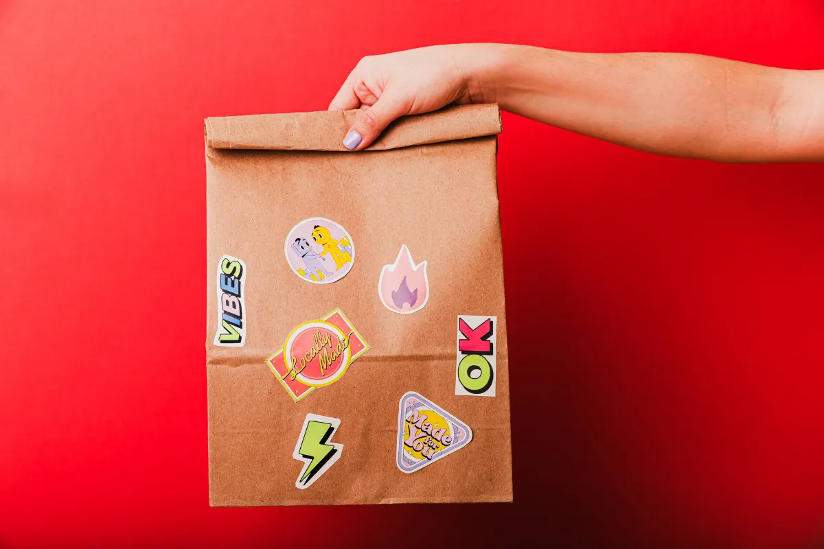 Sacola de papel kraft personalizada com adesivos divertidos, representando a identidade visual criativa de uma loja de salgados moderna e descolada.