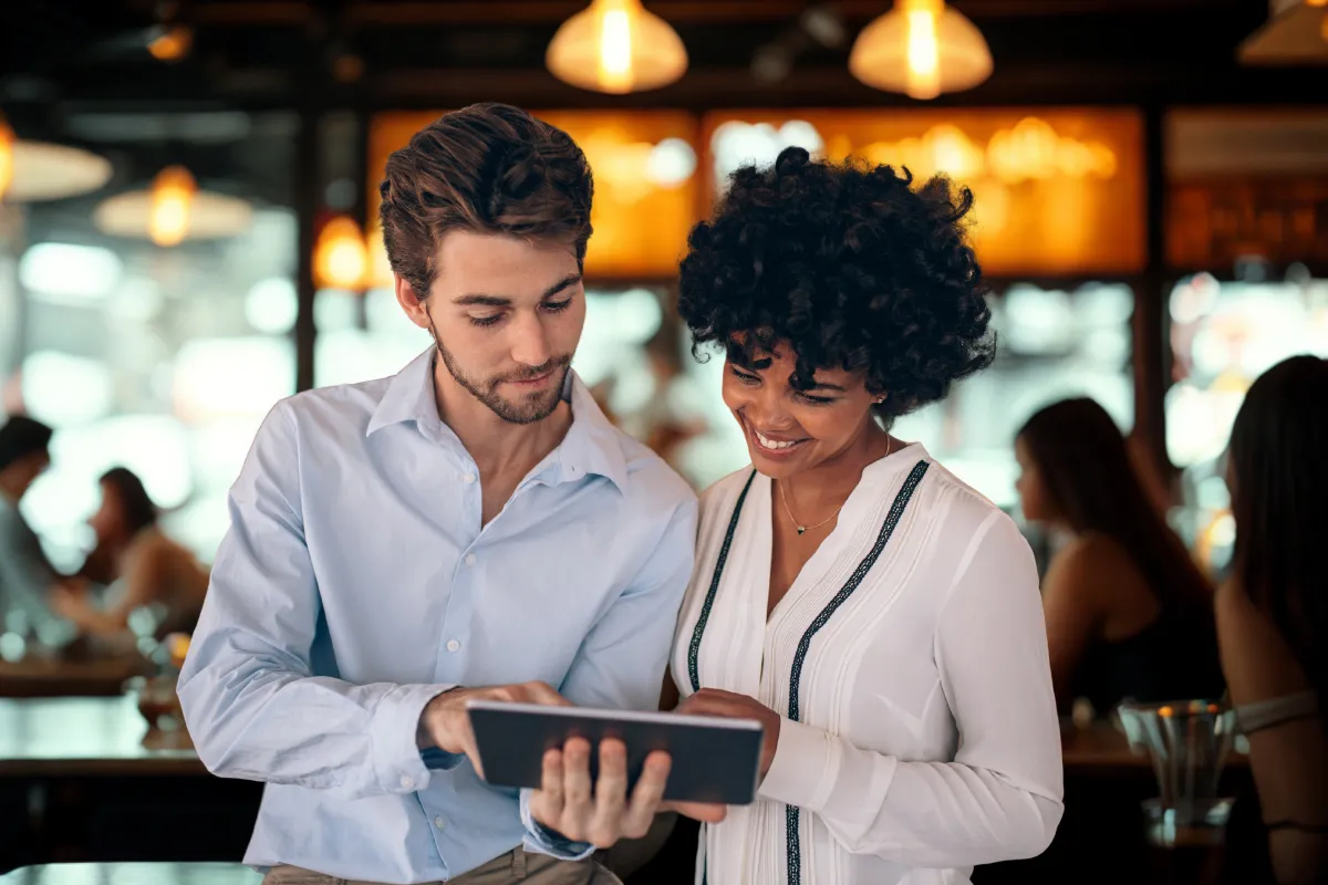 Gestores de restaurante analisando dados no tablet em ambiente movimentado, representando o uso da tecnologia para entender os horários de pico do restaurante.