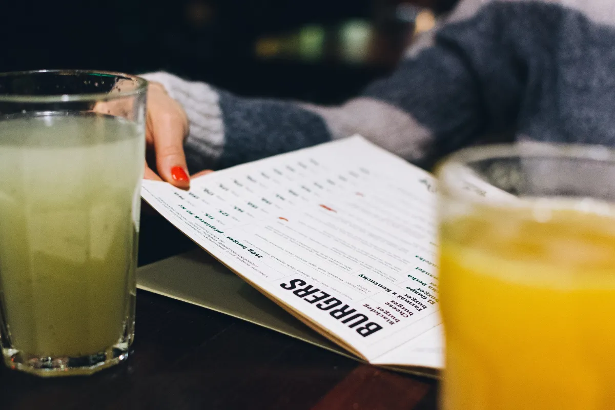 Pessoa folheando cardápio de hamburgueria ao lado de bebidas, representando a preparação e definição do menu para a inauguração de restaurante.
