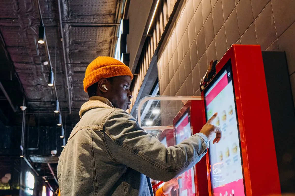 Cliente interagindo com totem de autoatendimento em restaurante fast food, ilustrando cardápio automatizado e moderno.