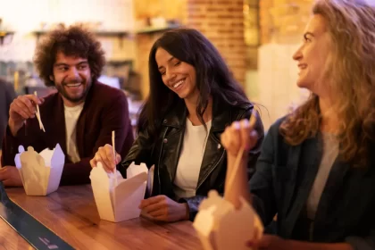 Grupo de amigos se divertindo enquanto comem comida oriental em embalagens para viagem — imagem que reforça nomes criativos e urbanos para deliverys.