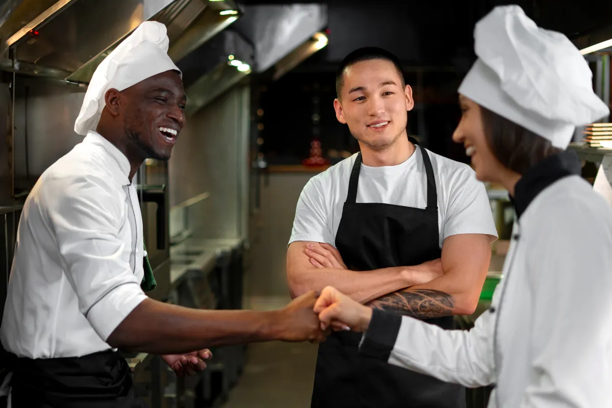 Equipe de cozinha interagindo de forma descontraída, ilustrando ajuste de escala e integração da equipe em momentos de alta ou baixa sazonal.


