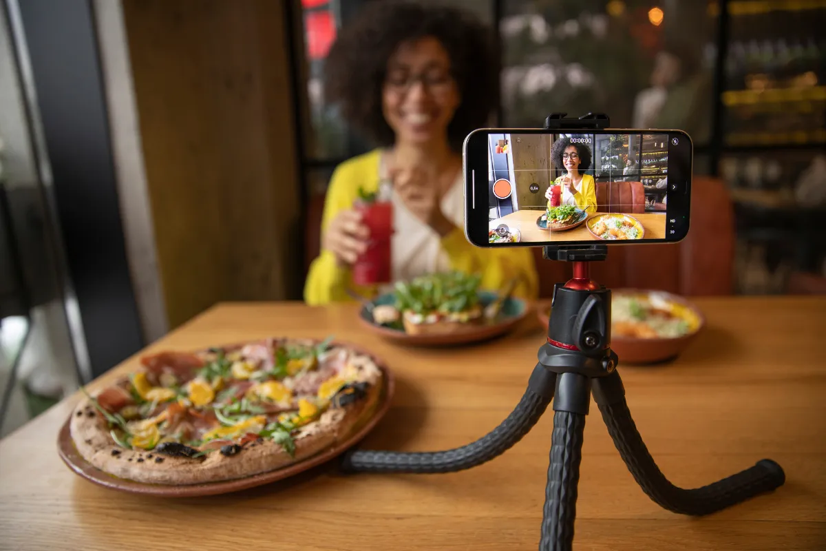  Influenciadora digital gravando vídeo de refeição em restaurante, representando ação de marketing sazonal para atrair público em diferentes períodos.