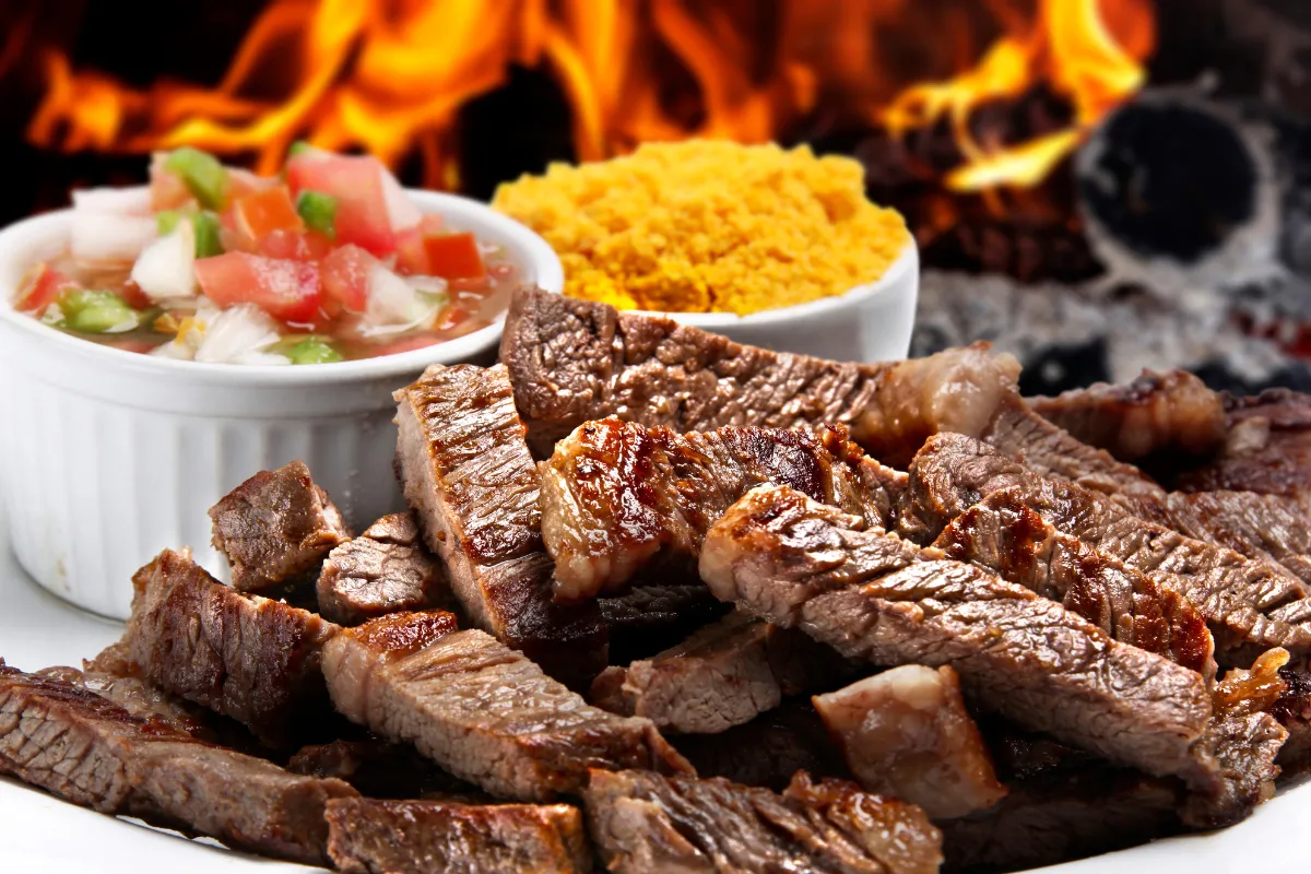 Churrasco na brasa servido em tiras com farofa amarela e vinagrete, prato clássico ideal para cardápios de Dia dos Pais em restaurantes e delivery.