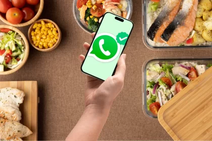 Mão segurando um celular com o ícone do WhatsApp em destaque, cercado por marmitas saudáveis e bem apresentadas.