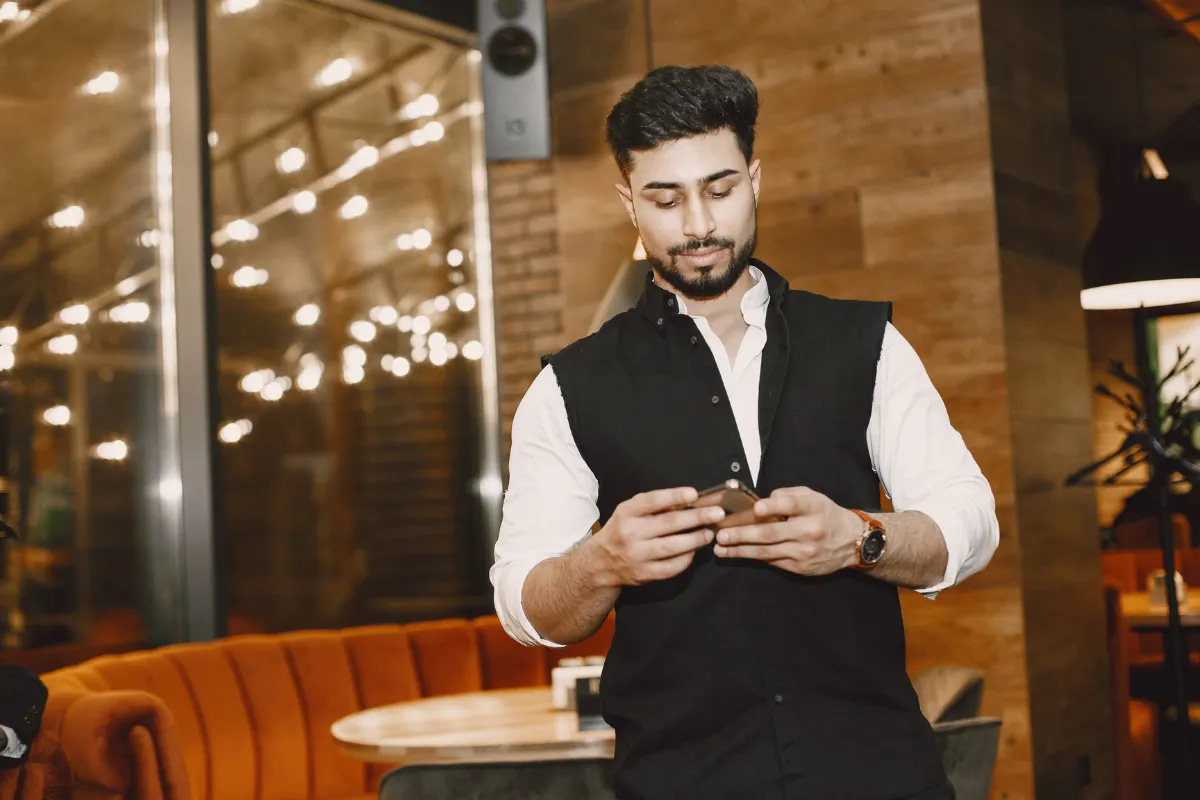 Profissional de restaurante utilizando celular no salão, representando o uso do app para garçom para controle de mesas e pedidos em tempo real.