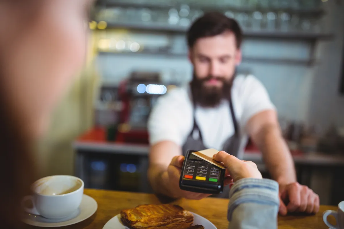Cliente realizando pagamento com cartão em maquininha POS no balcão de cafeteria, simbolizando a integração entre PDV e maquininhas para agilidade e segurança nas transações.