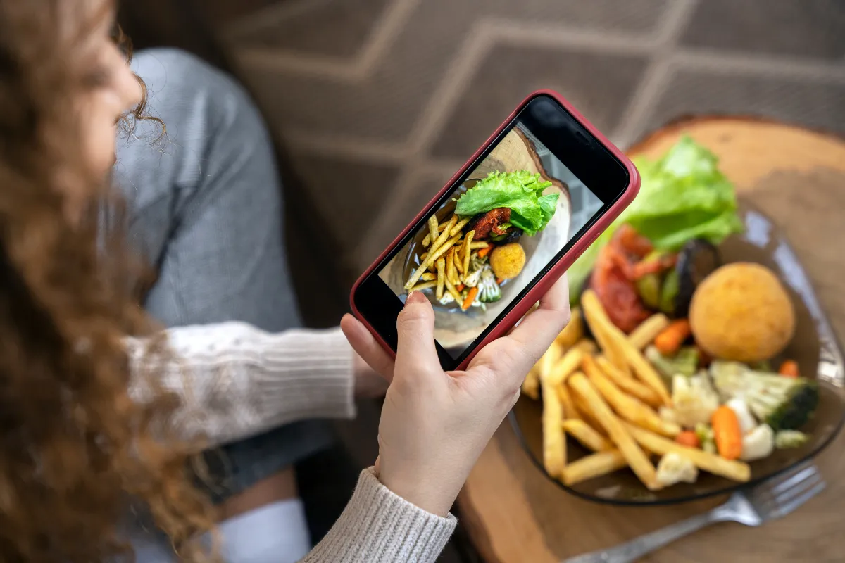 Pessoa tirando foto de marmita com batata frita e salada usando o celular, para divulgar nas redes sociais ou WhatsApp.