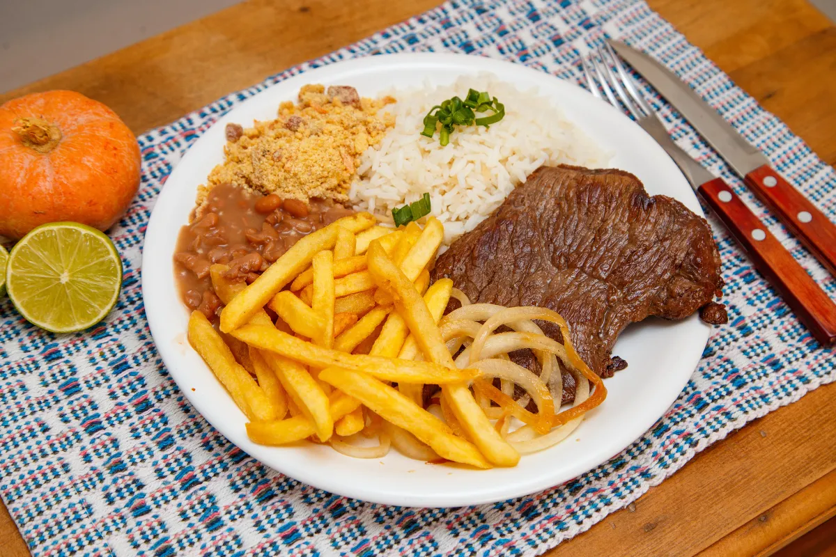 Prato feito brasileiro com arroz, feijão, bife, batata frita e farofa servido em mesa rústica — ideal para nomes que remetem à comida caseira e regional.