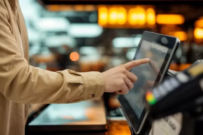 Pessoa tocando na tela de um terminal de autoatendimento para fazer pedido e pagamento em restaurante.