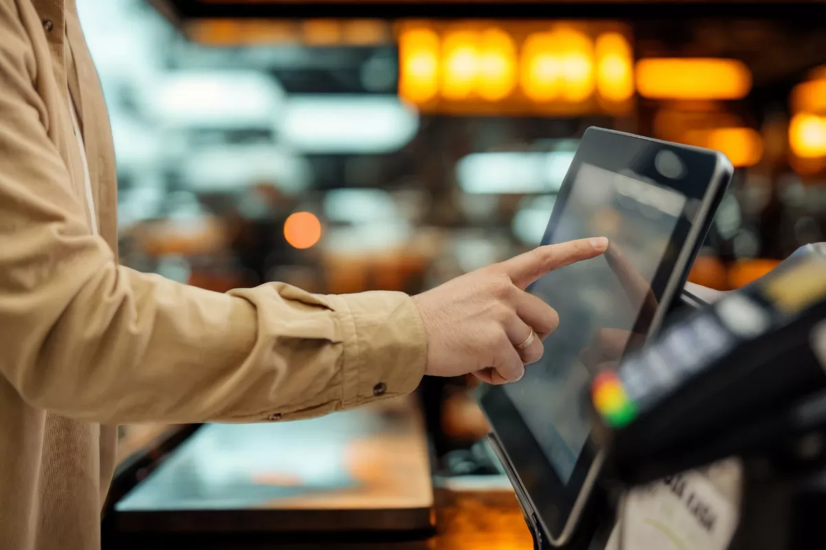Pessoa tocando na tela de um terminal de autoatendimento para fazer pedido e pagamento em restaurante.