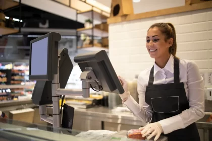 Atendente sorridente operando um sistema de PDV moderno em um balcão de atendimento, com duas telas integradas para registrar pedidos e gerenciar vendas em tempo real.