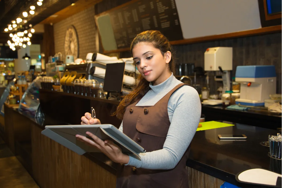 Funcionária de restaurante usando tablet para registrar pedidos, representando a automação e integração de dados com sistema ERP para restaurantes.