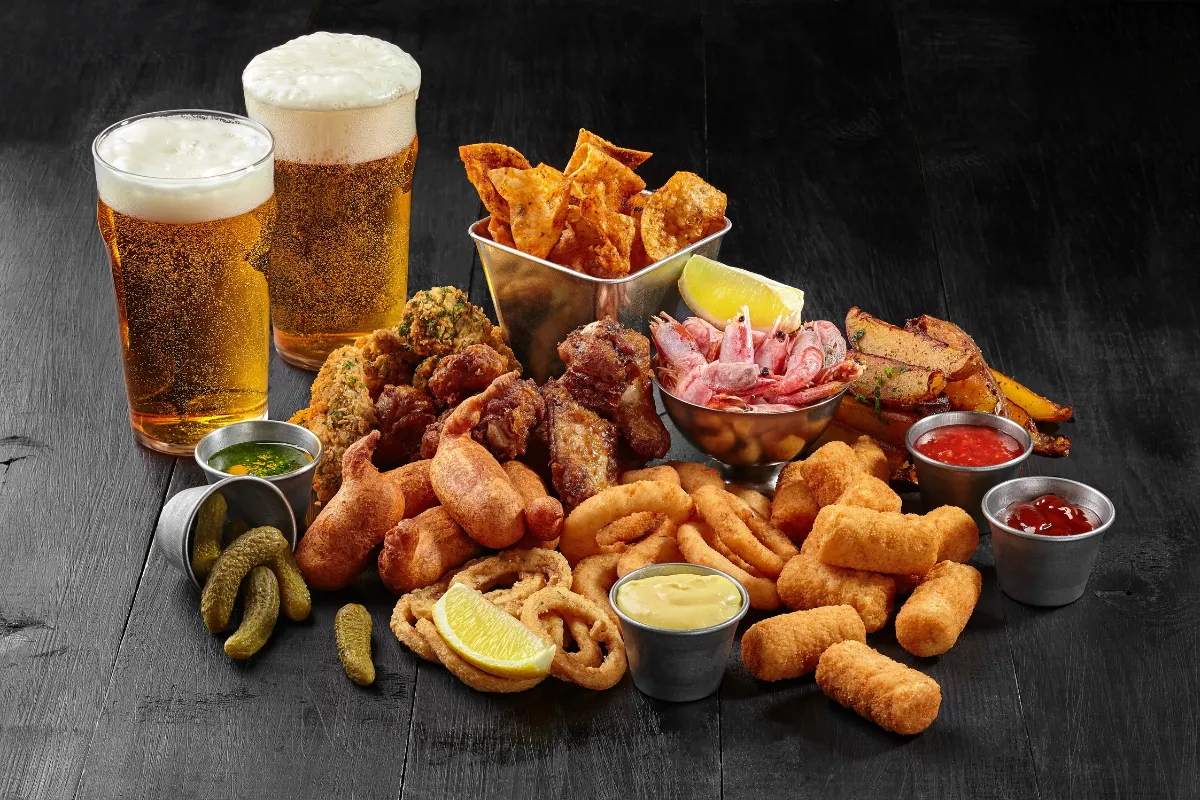 Mesa com petiscos variados e dois copos de chope gelado, representando a rotina intensa de uma petiscaria e a importância de um sistema ágil para organizar pedidos.