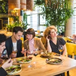 Grupo de clientes sendo atendido por garçonete em restaurante cheio, representando período de alta demanda no food service.