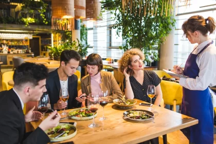Grupo de clientes sendo atendido por garçonete em restaurante cheio, representando período de alta demanda no food service.