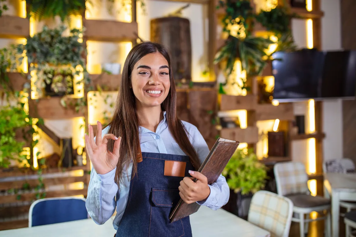 Gerente de restaurante sorridente com cardápio em mãos, simbolizando gestão proativa diante das variações sazonais de movimento.
