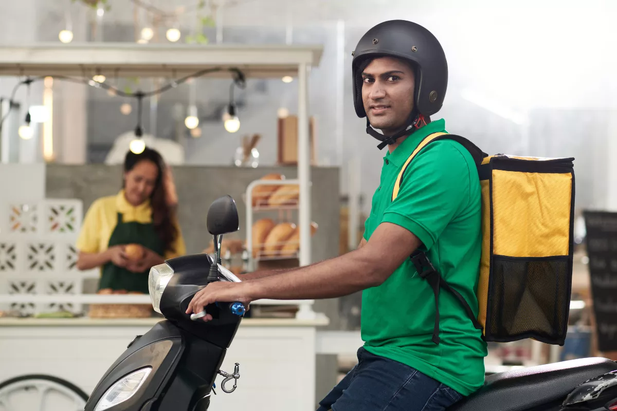 Entregador de restaurante em motocicleta com mochila térmica amarela, representando a importância do delivery para aumentar o ticket médio.
