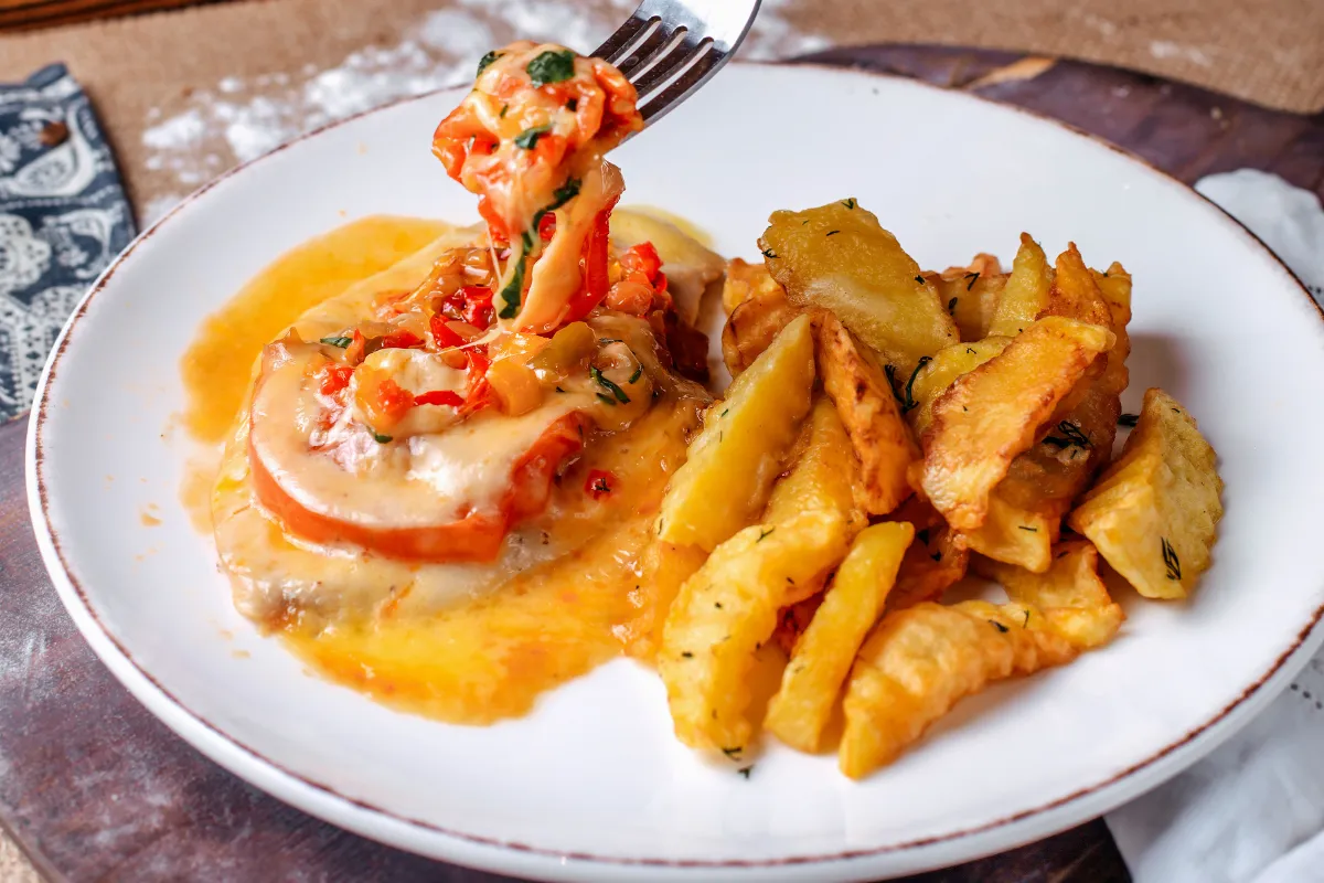 Prato servido com carne gratinada, legumes e batatas rústicas, ilustrando a padronização de porções como estratégia para evitar desperdício de alimentos no restaurante.