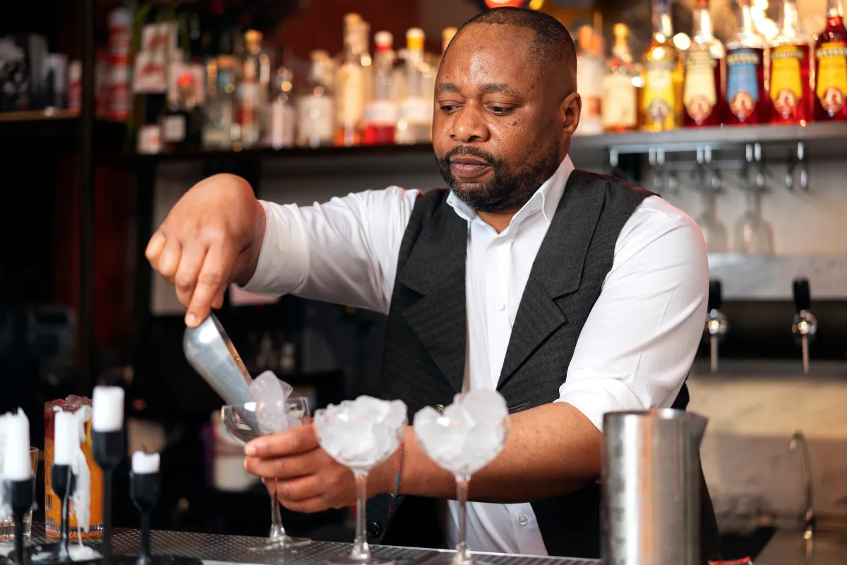 Bartender preparando drinks com gelo no bar do restaurante, exemplificando o papel do barman na criação de bebidas e na experiência do cliente.