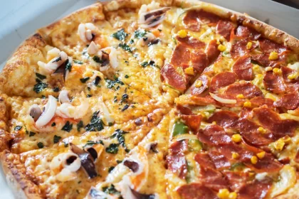 Pizza meio a meio com dois sabores diferentes, frutos do mar e calabresa com milho, ilustrando a dúvida comum sobre como cobrar corretamente a pizza dois sabores conforme a lei.