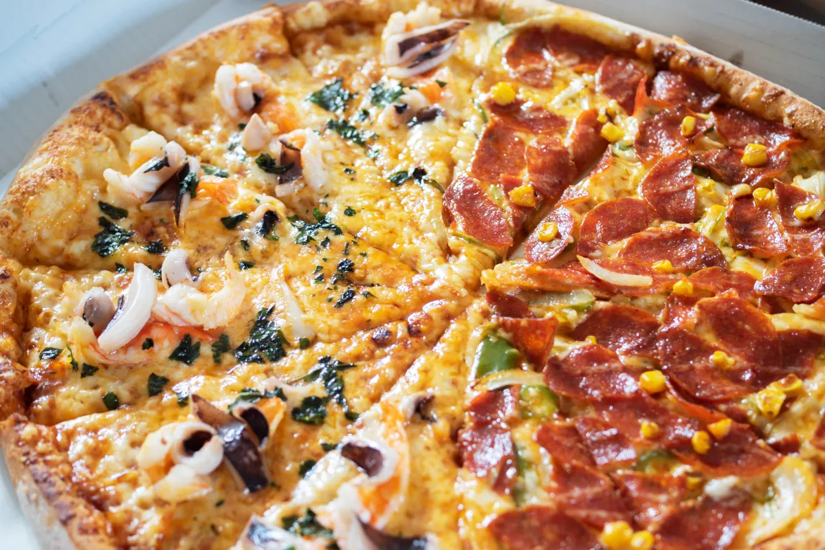 Pizza meio a meio com dois sabores diferentes, frutos do mar e calabresa com milho, ilustrando a dúvida comum sobre como cobrar corretamente a pizza dois sabores conforme a lei.