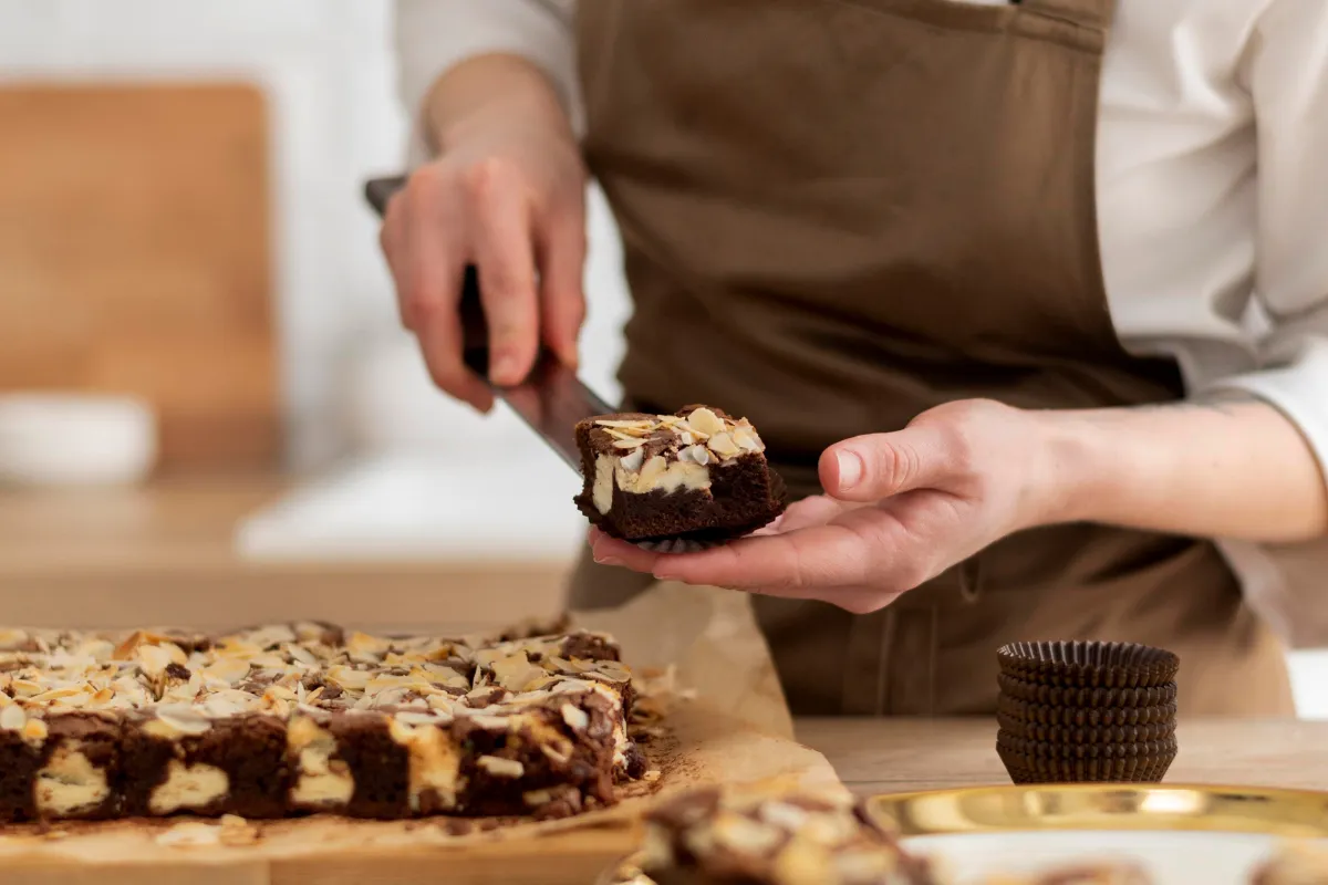 Close de uma confeiteira cortando um pedaço de brownie, simbolizando a importância do controle de porções e da ficha técnica para uma doceria mais lucrativa.