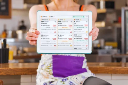 Mulher segura tablet com a Central de Delivery do ControleNaMão na tela, diante do balcão de um restaurante.