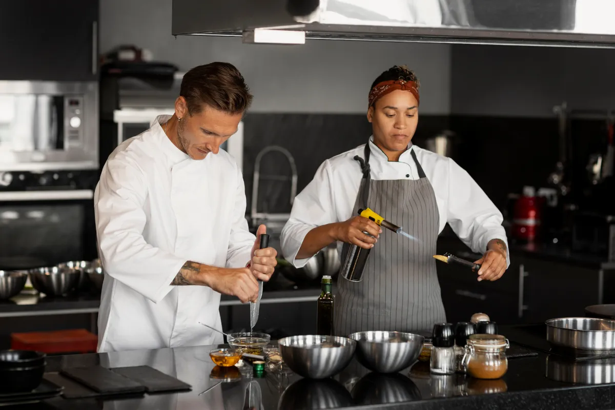 Dois chefs de cozinha preparando pratos em uma cozinha profissional, exemplificando a liderança e execução na hierarquia de um restaurante.