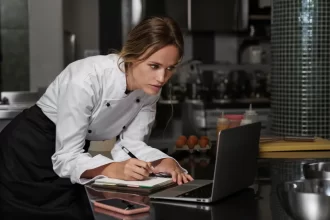 Chef de restaurante consultando informações no computador e anotando dados fiscais, exemplificando a importância do controle financeiro na escolha da alíquota do Simples Nacional.