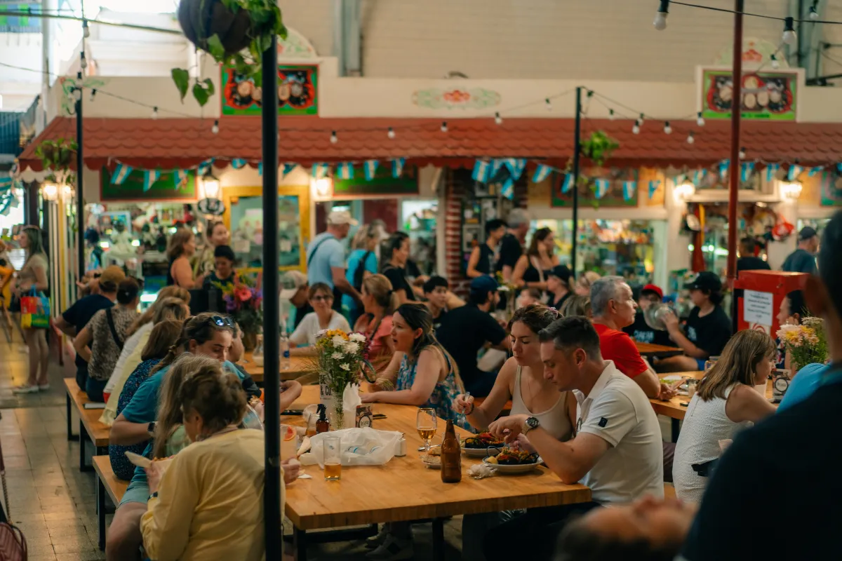  Vista panorâmica de um restaurante ou praça de alimentação cheia, com mesas e pessoas movimentadas. A imagem ilustra uma operação de restaurante durante um pico de movimento, como o da Black Friday, com o objetivo de evitar filas e confusão.
