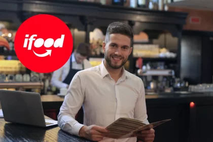 Empresário de restaurante sorrindo com cardápio em mãos, ao lado de um notebook, com o logo do iFood em destaque — contexto sobre investir no iFood ADS.