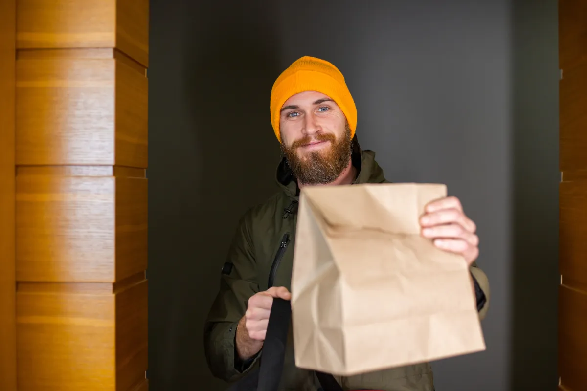 Entregador de touca laranja segurando uma embalagem de papel cartão resinado/kraft